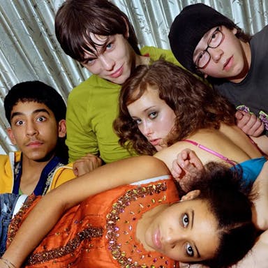 A group of young people tangled up and laying on top of each other looking at the camera