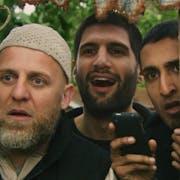 Three men huddled together looking through a gap in the fence looking surprised