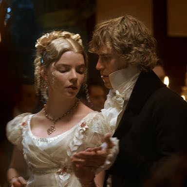 A blonde woman and a blond man in period costume dancing closely in a dark candlelit room