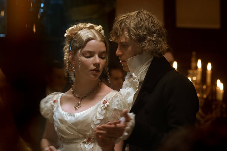 A blonde woman and a blond man in period costume dancing closely in a dark candlelit room