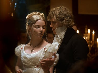 A blonde woman and a blond man in period costume dancing closely in a dark candlelit room