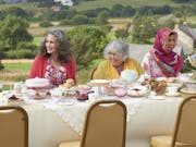 Group of women sit outside in the countryside at a table covered with cakes and teapots