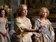 A blonde woman in expensive period clothing, holding out a pink rose, flanked by other women