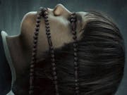 Spooky image of a young person with rosary beads wrapped around eyes and mouth