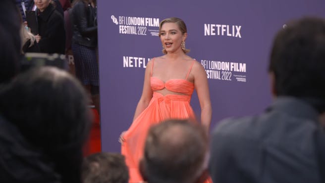 Woman in a peach coloured dress poses for photographs on a red carpet.