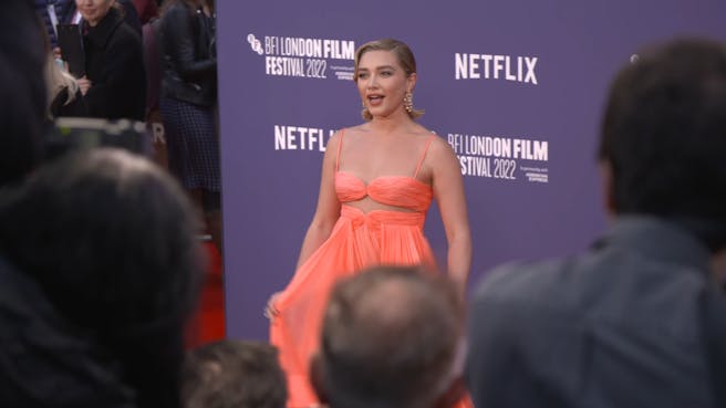 Woman in a peach coloured dress poses for photographs on a red carpet.