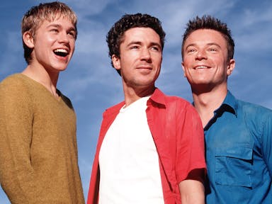 Three white men smiling with a bright blue sky behind them