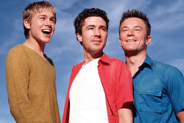 Three white men smiling with a bright blue sky behind them