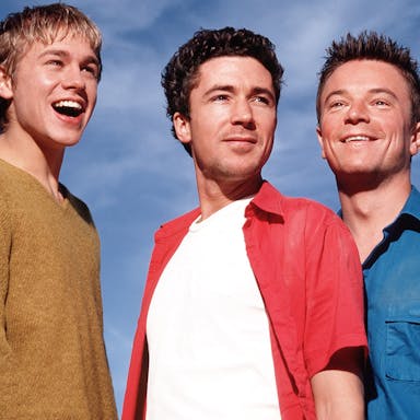 Three white men smiling with a bright blue sky behind them