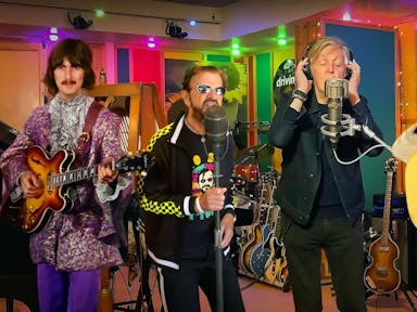 A colour recording studio with four white men, two real life older men (Ringo and Paul McCartney) flanked by digital young men with guitars (George Harrison, and John Lennon)