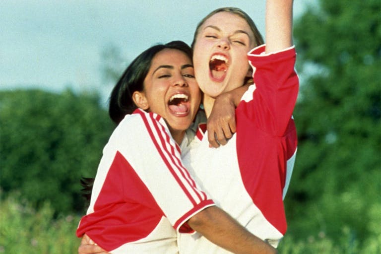 Two young women in a triumphant embrace, arm in the air, both wearing white and red football kit