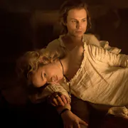 Blonde woman in an old-fashioned white nightgown lies across a man