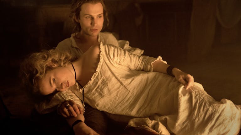 Blonde woman in an old-fashioned white nightgown lies across a man