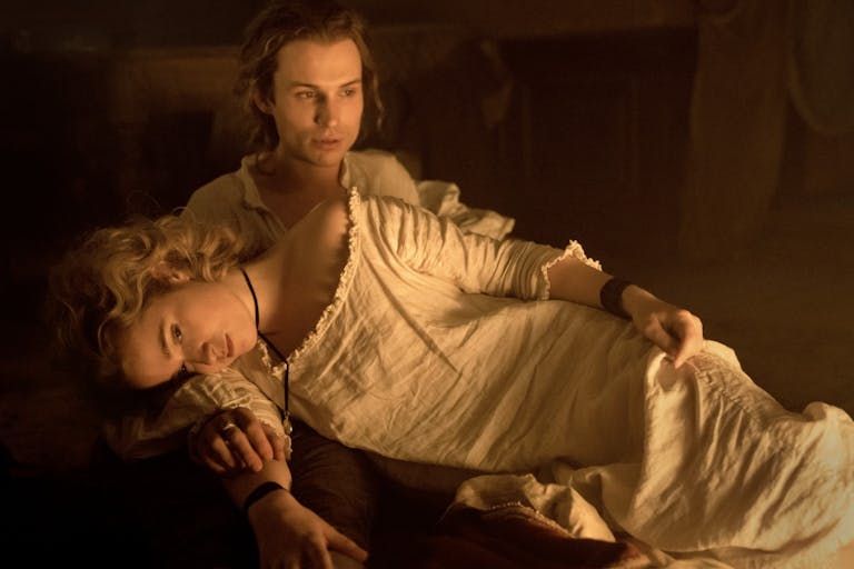 Blonde woman in an old-fashioned white nightgown lies across a man