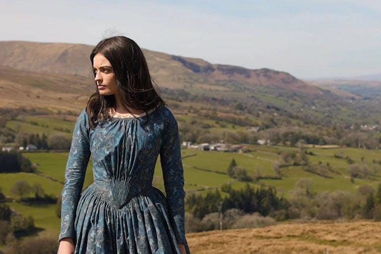 Woman with dark hair in period costume against a countryside backdrop.