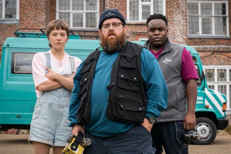 A white woman, white man and Black man stand looking determined in front of a turquoise van