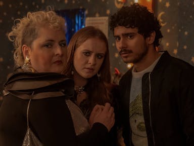 A white woman with curly blonde mohawk, a young white woman with ginger hair and a brown man with short curly hair and bomber jacket