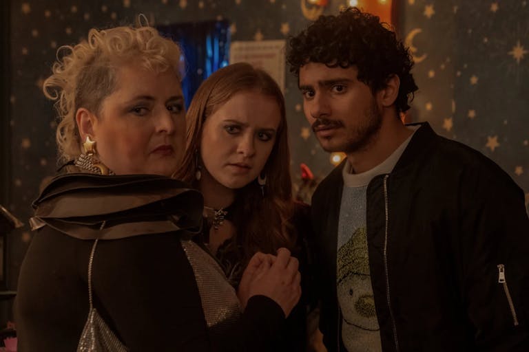 A white woman with curly blonde mohawk, a young white woman with ginger hair and a brown man with short curly hair and bomber jacket