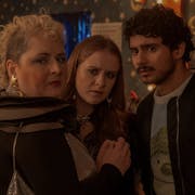 A white woman with curly blonde mohawk, a young white woman with ginger hair and a brown man with short curly hair and bomber jacket
