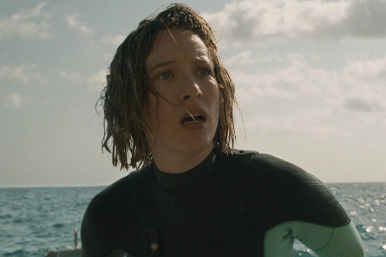 Woman with wet hair in a wetsuit in the sea, looking into the distance shocked