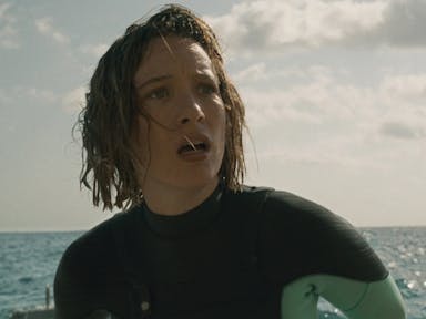 Woman with wet hair in a wetsuit in the sea, looking into the distance shocked