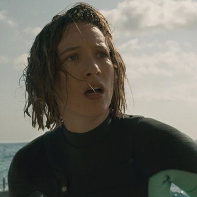 Woman with wet hair in a wetsuit in the sea, looking into the distance shocked