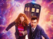 A red headed white woman and a dark haired white man in long blue coat, run away from cosmic galaxy activity with the TARDIS, a blue police box, in the background
