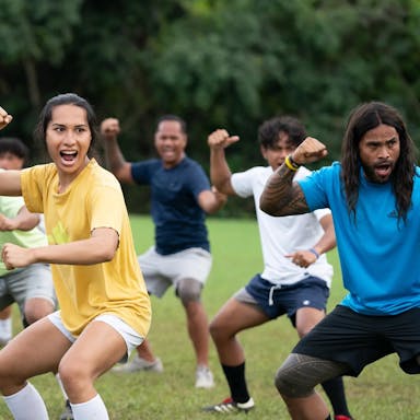 American Samoan football team of men and a trans woman performing the Haka in a green training field