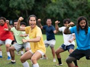 American Samoan football team of men and a trans woman performing the Haka in a green training field