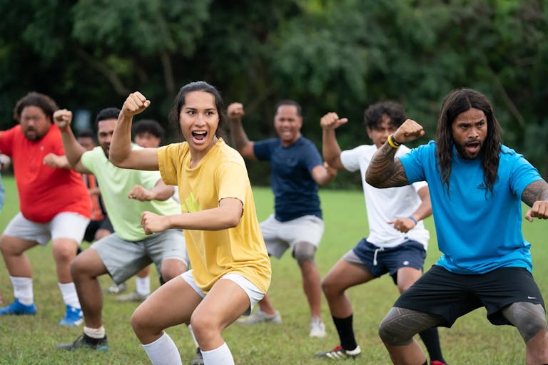 American Samoan football team of men and a trans woman performing the Haka in a green training field