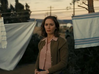 A white woman with short windswept brown hair looking concerned and thoughtful, with white sheets pegged on a clothes line behind her