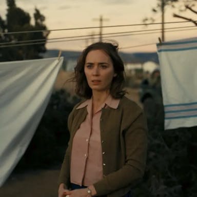 A white woman with short windswept brown hair looking concerned and thoughtful, with white sheets pegged on a clothes line behind her