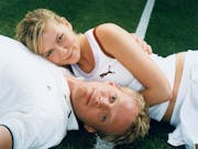 A blonde woman laying her head on a blond man's chest as he lays the opposite way to her, both in tennis clothing