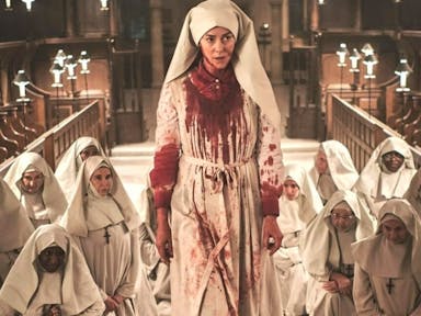 Group of nuns in white habits in a church, one of them covered in blood