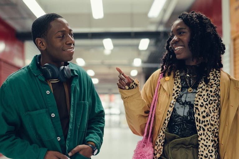 A young man and a woman walk through a shopping centre smiling at each other