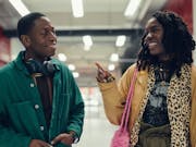A young man and a woman walk through a shopping centre smiling at each other