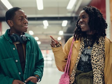 A young Black man and a young Black woman walk through a colourful indoor market in Peckham