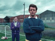 Two men looking serious with arms folded standing on a football pitch next to a small practice goal