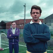 Two men looking serious with arms folded standing on a football pitch next to a small practice goal