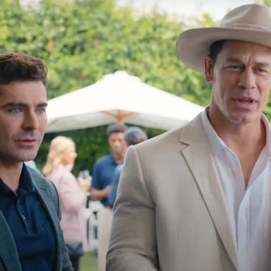 Two white men one in a dark casual suit, the other in a white suit and white cowboy hat, at a garden party