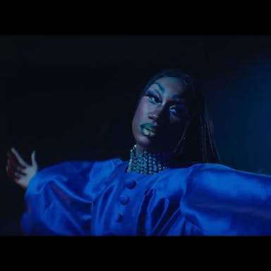 A young Black drag queen in a flouncy deep blue dress dancing, looking ethereal
