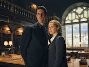 A white man and woman in dark suits stand in a grand library