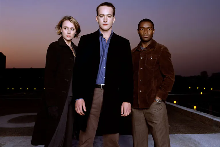 A white woman, white man and Black man stand looking mysterious and serious