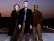 A white woman, white man and Black man stand looking mysterious and serious