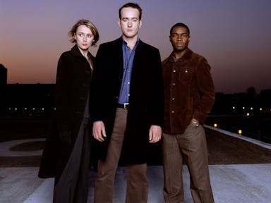A white woman, white man and Black man stand looking mysterious and serious 