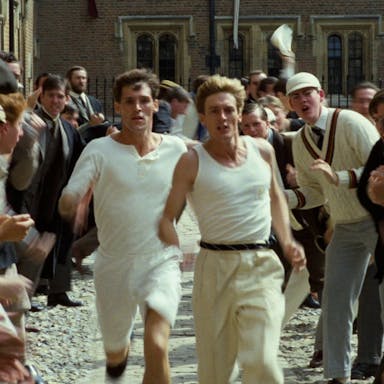 Two men dressed in white running through a crowd of people cheering them on