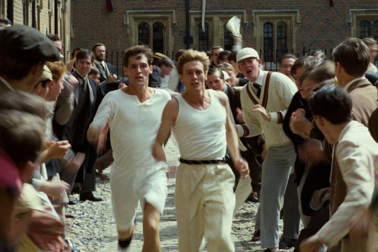 Two men dressed in white running through a crowd of people cheering them on