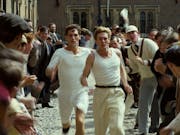 Two men dressed in white running through a crowd of people cheering them on