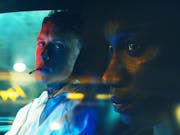 Close up of a thuggish looking young white man with neck tattoos smoking a cigarette staring at a young Black man looking off into the distance