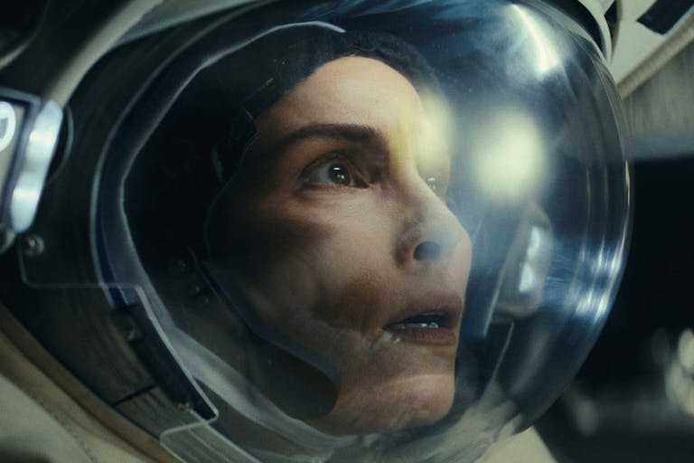 Close up of a white woman in space in an astronaut's clothing and helmet looking shocked